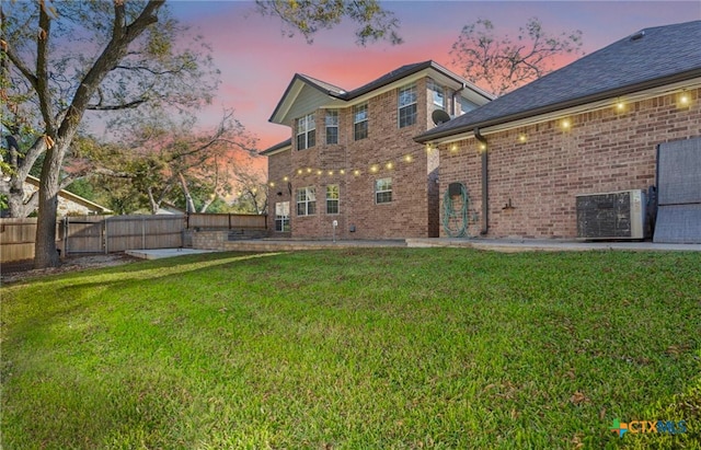 back house at dusk with central AC unit and a yard