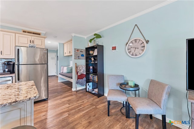 kitchen featuring light stone counters, crown molding, light hardwood / wood-style flooring, cream cabinetry, and stainless steel fridge