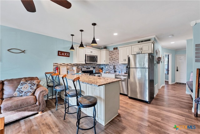 kitchen with light stone counters, kitchen peninsula, hanging light fixtures, a breakfast bar, and appliances with stainless steel finishes