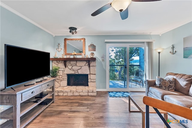 living room with a stone fireplace, hardwood / wood-style floors, ceiling fan, and crown molding