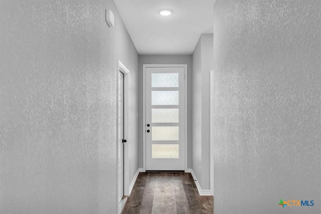 doorway featuring baseboards, dark wood-style flooring, and a textured wall