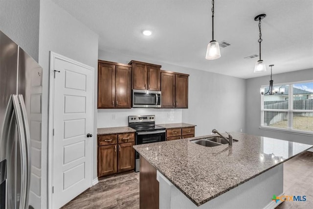 kitchen featuring light stone counters, pendant lighting, appliances with stainless steel finishes, a kitchen island with sink, and a sink