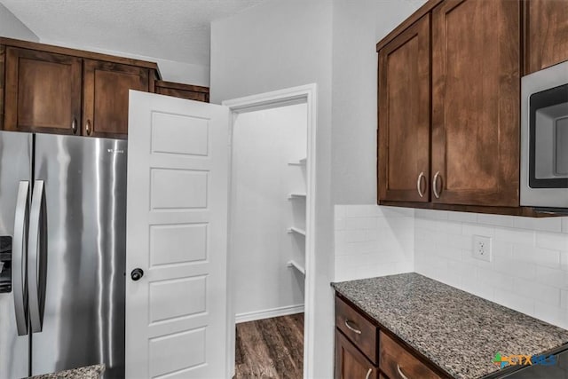 kitchen with tasteful backsplash, a textured ceiling, appliances with stainless steel finishes, and dark stone countertops