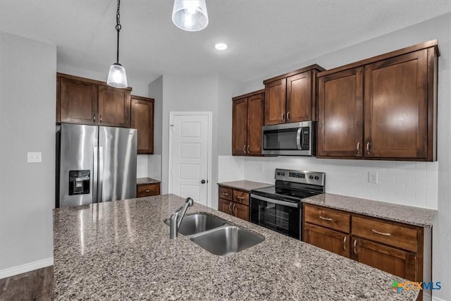 kitchen featuring stainless steel appliances, hanging light fixtures, a sink, and light stone countertops