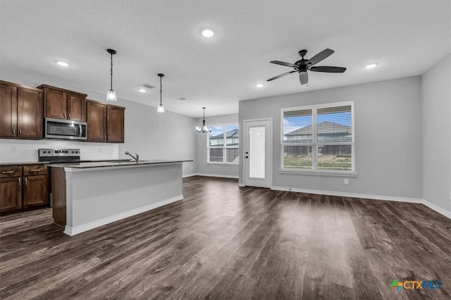 kitchen with a center island with sink, appliances with stainless steel finishes, dark wood-style flooring, hanging light fixtures, and ceiling fan with notable chandelier