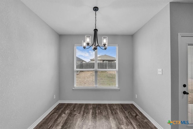 unfurnished dining area with baseboards, dark wood finished floors, and a notable chandelier