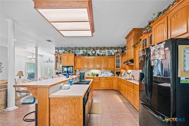 kitchen featuring under cabinet range hood, light countertops, a sink, decorative columns, and black appliances