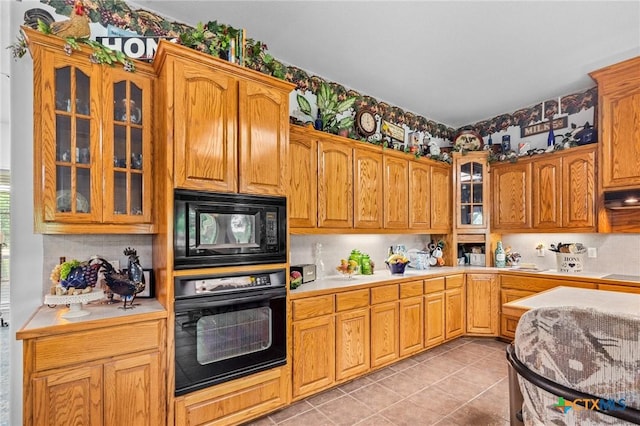 kitchen with glass insert cabinets, light countertops, backsplash, and black appliances