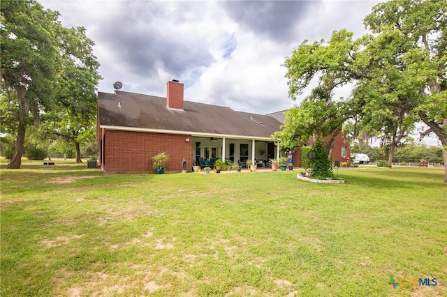 rear view of property with a patio area, a lawn, a chimney, brick siding, and ceiling fan
