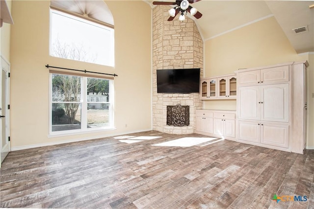 unfurnished living room featuring high vaulted ceiling, a stone fireplace, dark wood-type flooring, a ceiling fan, and visible vents