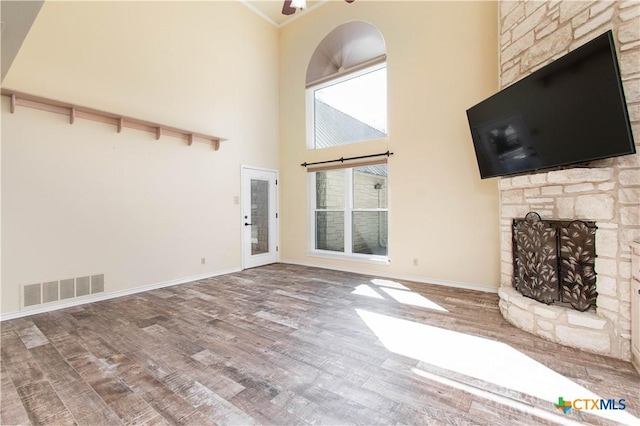 unfurnished living room with a stone fireplace, wood finished floors, visible vents, and baseboards