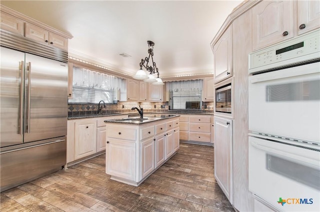 kitchen with dark wood finished floors, dark countertops, an island with sink, built in appliances, and pendant lighting