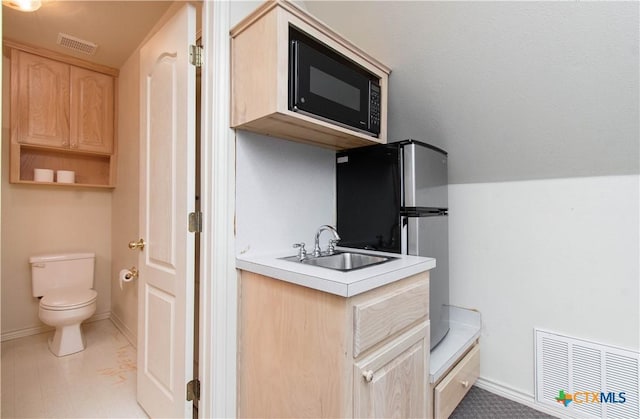 kitchen featuring black microwave, a sink, visible vents, light countertops, and light brown cabinetry