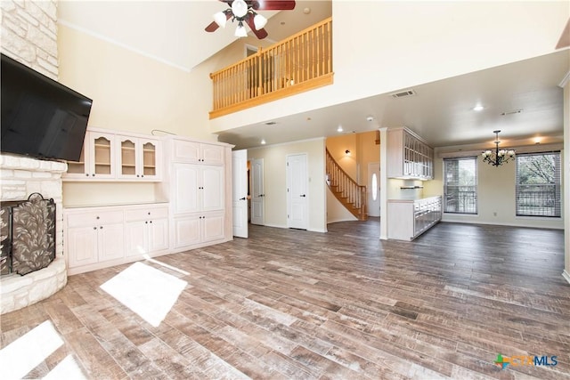 unfurnished living room with ceiling fan with notable chandelier, wood finished floors, visible vents, baseboards, and stairs