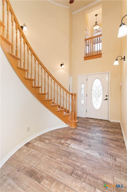 foyer featuring ornamental molding, stairway, wood finished floors, and baseboards