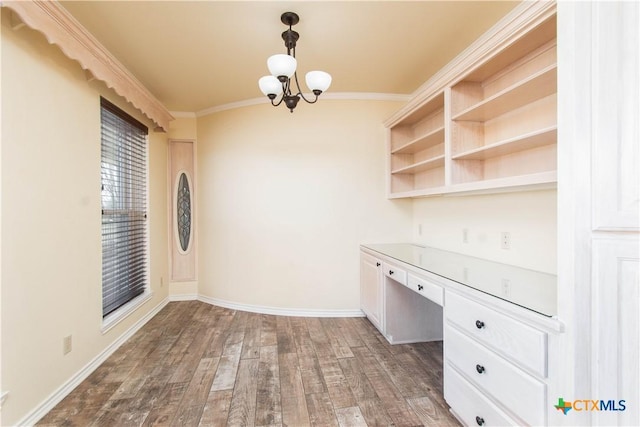 unfurnished office featuring crown molding, dark wood-type flooring, baseboards, built in desk, and an inviting chandelier