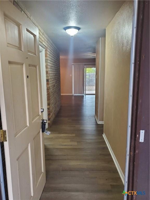 corridor featuring dark wood-type flooring, brick wall, and a textured ceiling