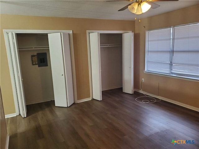 unfurnished bedroom featuring ceiling fan, dark hardwood / wood-style floors, and two closets