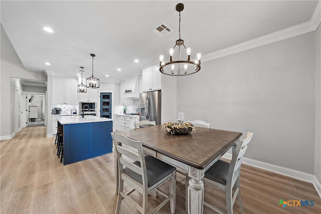 dining space featuring sink, light wood-type flooring, an inviting chandelier, and crown molding