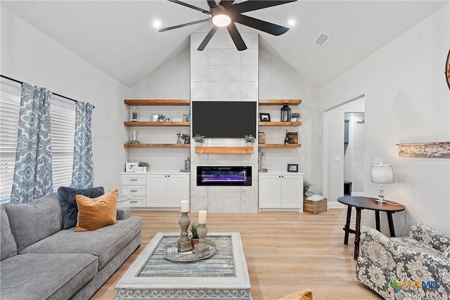 living room featuring a tiled fireplace, ceiling fan, vaulted ceiling, and light hardwood / wood-style flooring