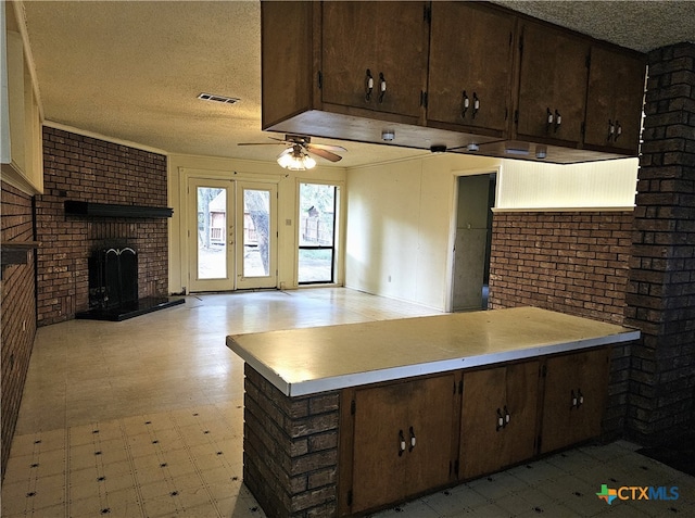 kitchen with french doors, a brick fireplace, a textured ceiling, kitchen peninsula, and brick wall