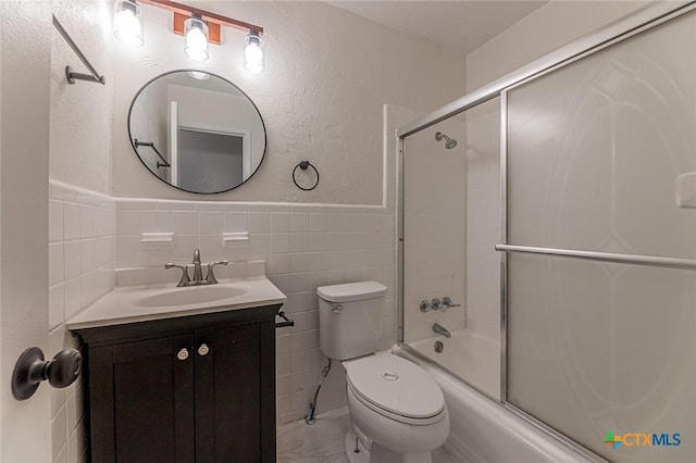 full bathroom with shower / bath combination with glass door, vanity, toilet, and tile walls