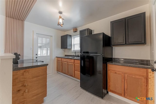 kitchen featuring dark stone countertops, stove, black refrigerator, and sink