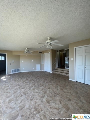 unfurnished living room featuring ceiling fan and a textured ceiling