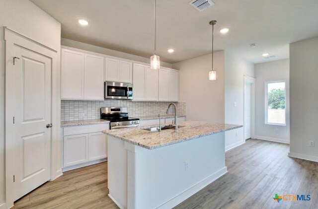 3625 Meteor Rd, New Braunfels, TX 78130 - kitchen featuring appliances with stainless steel finishes, a sink, decorative backsplash, light wood-style flooring, and an island with sink