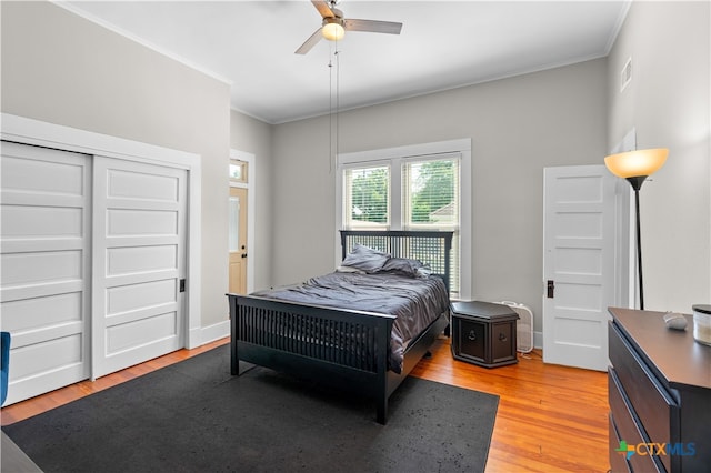 bedroom featuring hardwood / wood-style flooring, ornamental molding, ceiling fan, and a closet