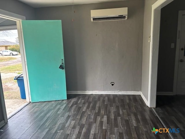 spare room with wood finished floors, an AC wall unit, and baseboards