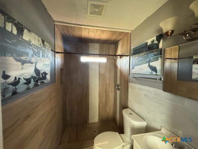 bathroom featuring a shower stall, toilet, visible vents, and tile walls
