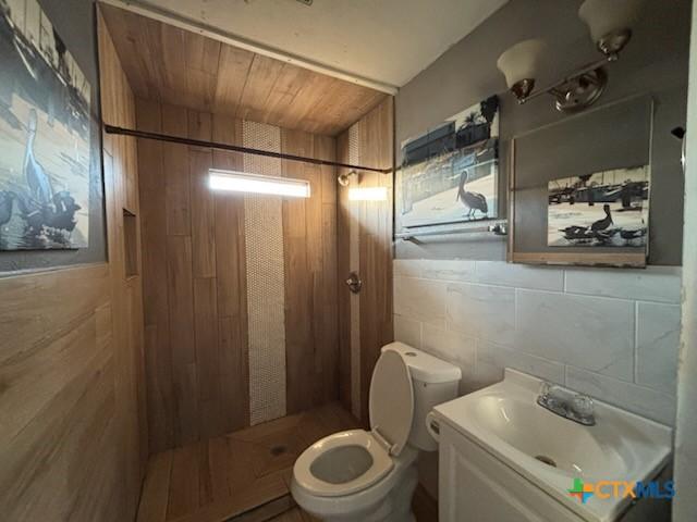 bathroom with toilet, tile walls, a stall shower, decorative backsplash, and vanity