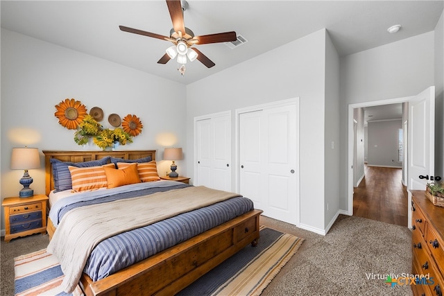 bedroom with ceiling fan, dark carpet, and two closets