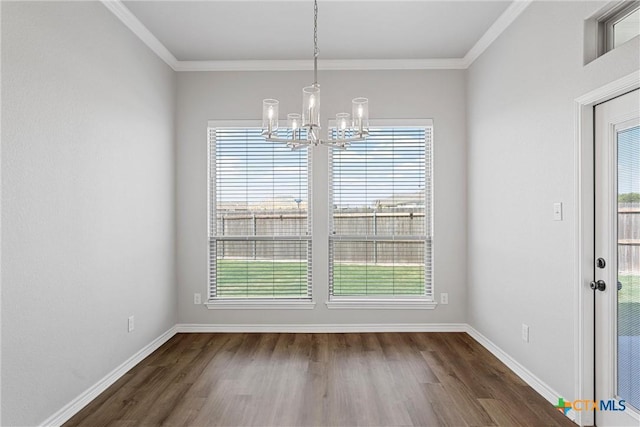 unfurnished dining area featuring dark wood-type flooring, plenty of natural light, crown molding, and an inviting chandelier