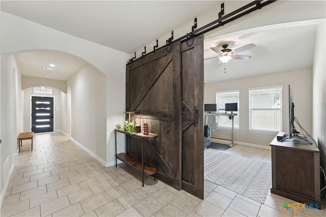 hallway featuring a wealth of natural light, light tile patterned floors, arched walkways, and baseboards