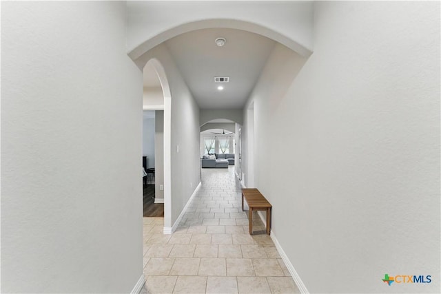 corridor with light tile patterned floors, baseboards, visible vents, and arched walkways