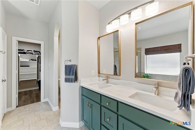 bathroom with a sink, a walk in closet, visible vents, and double vanity