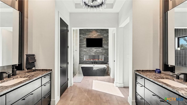 bathroom featuring an inviting chandelier, vanity, a washtub, and a fireplace