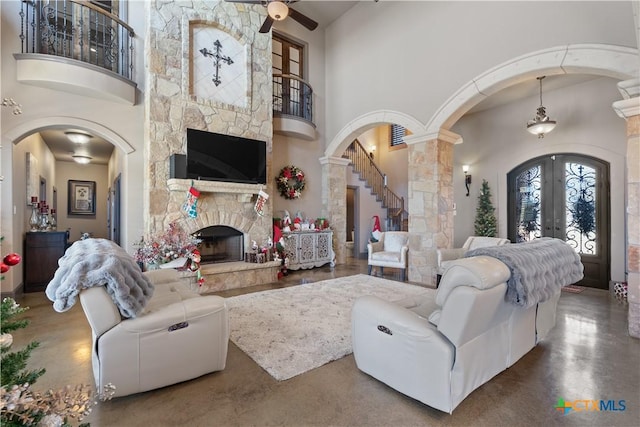 living room featuring a fireplace, a towering ceiling, decorative columns, and concrete floors