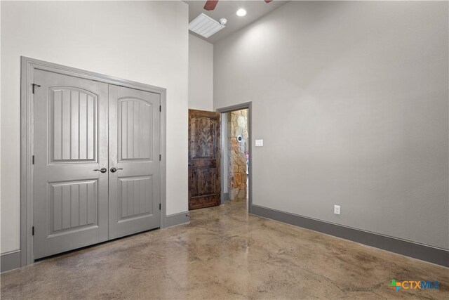 unfurnished bedroom with ceiling fan, concrete flooring, a high ceiling, and a closet