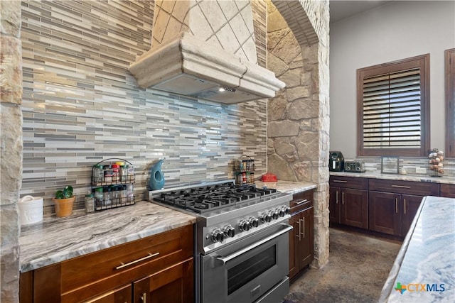 kitchen featuring tasteful backsplash, light stone counters, stainless steel stove, and custom range hood