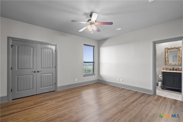 unfurnished bedroom featuring ceiling fan, sink, ensuite bathroom, and light hardwood / wood-style flooring