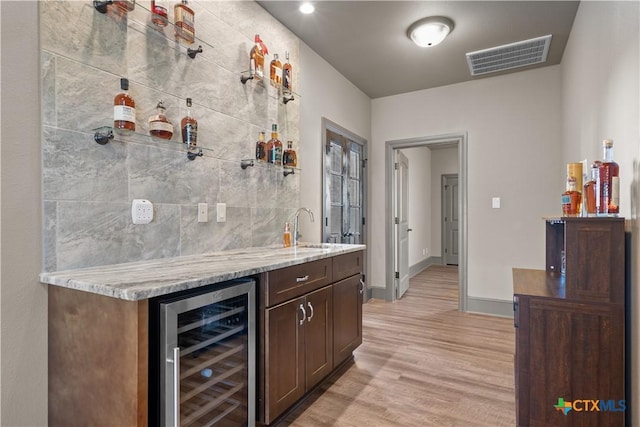 bar featuring light stone counters, dark brown cabinetry, beverage cooler, sink, and light hardwood / wood-style floors