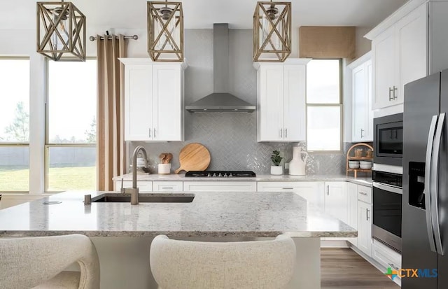 kitchen featuring wall chimney exhaust hood, a sink, backsplash, and stainless steel appliances
