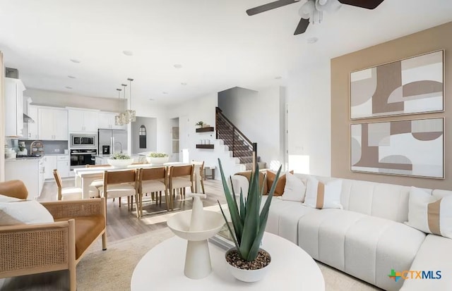 living room featuring light wood-type flooring, a ceiling fan, recessed lighting, and stairs