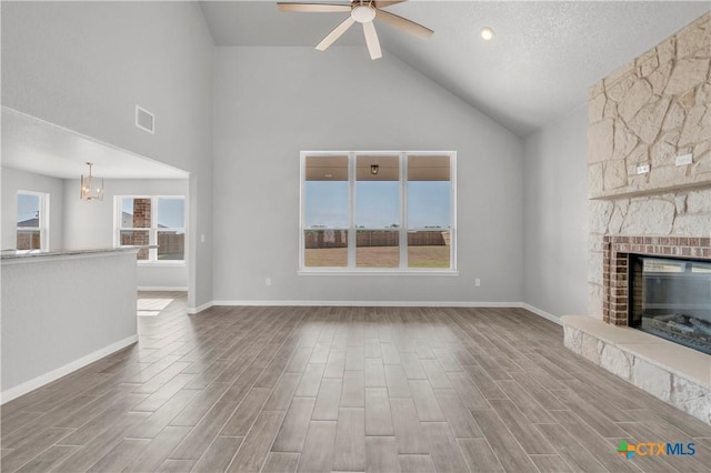unfurnished living room featuring wood finished floors, visible vents, a fireplace, high vaulted ceiling, and ceiling fan with notable chandelier