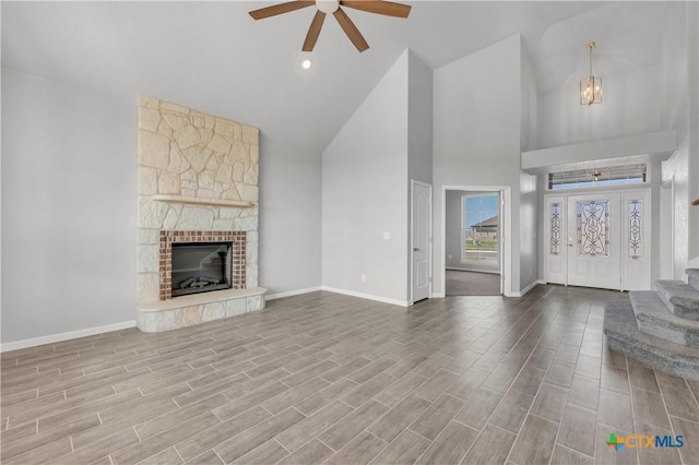 unfurnished living room featuring baseboards, a ceiling fan, stairs, a stone fireplace, and high vaulted ceiling