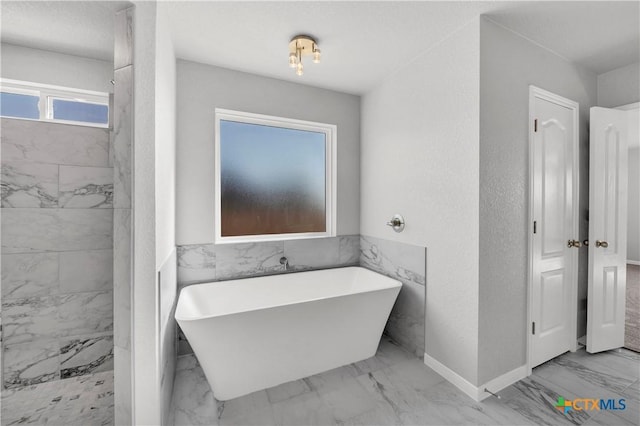 full bath with a freestanding tub, wainscoting, and marble finish floor