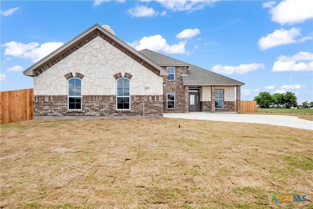 view of front of house featuring fence, a front lawn, roof with shingles, stone siding, and brick siding
